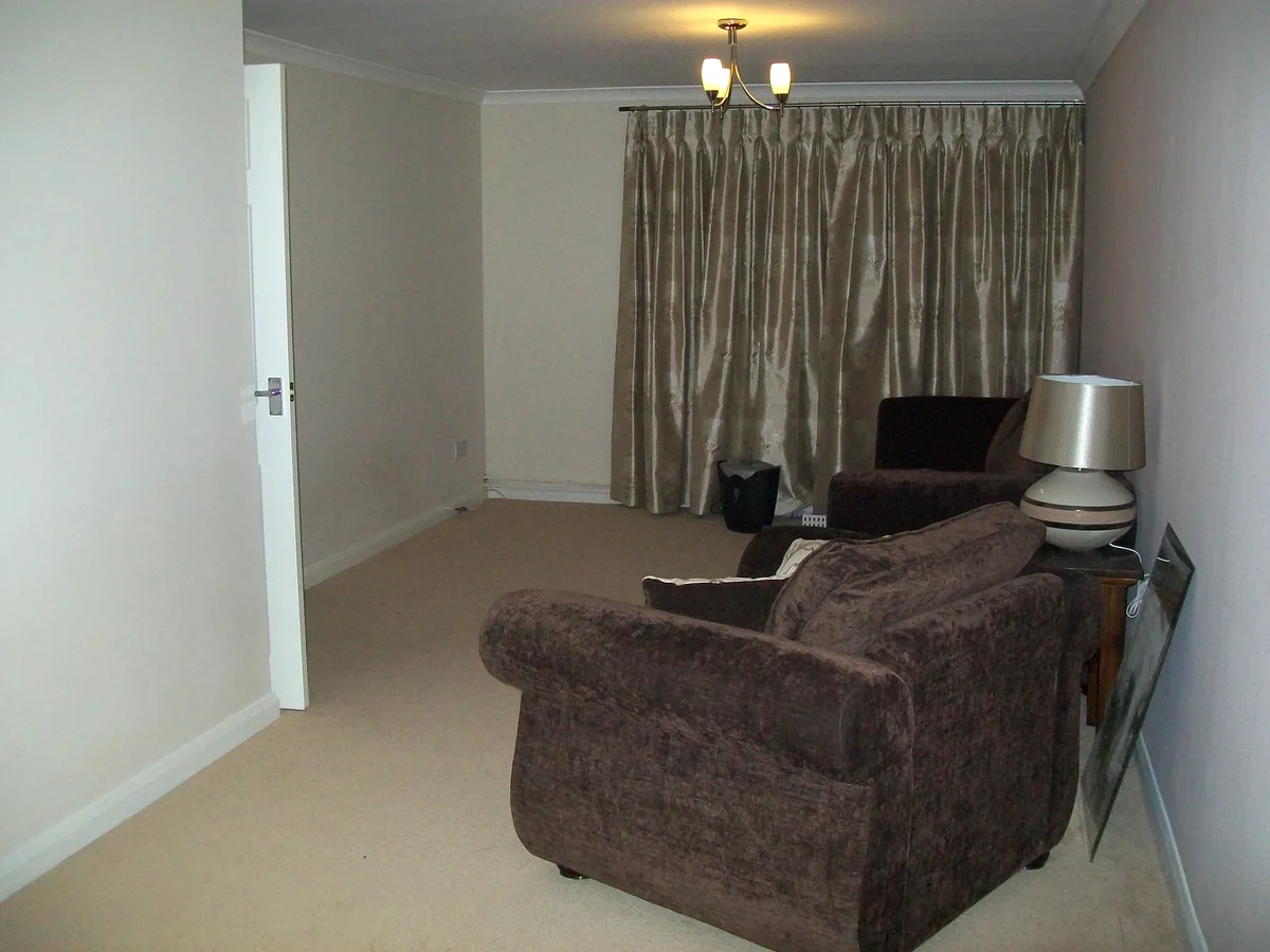 A quiet, tidy living room in an English house, with two armchairs, a table lamp and drawn curtains, partly cleared after the owners moved out