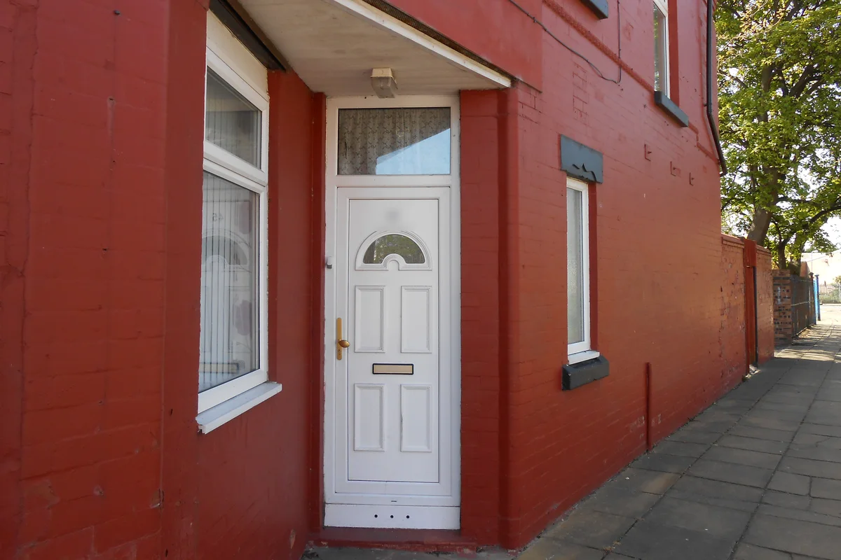 White uPVC front door with a brass handle and letterbox on a red-brick end-terrace house in England